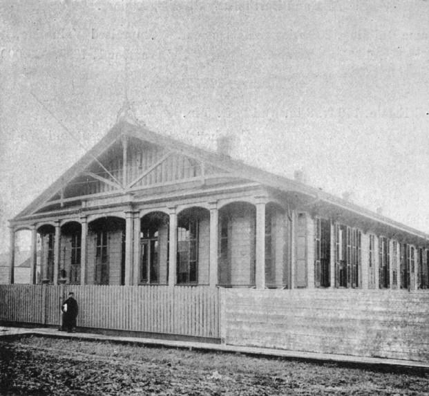 Black-and-White photograph of McDonogh No. 5. A man stands outside a picket fence dividing the school from the street.