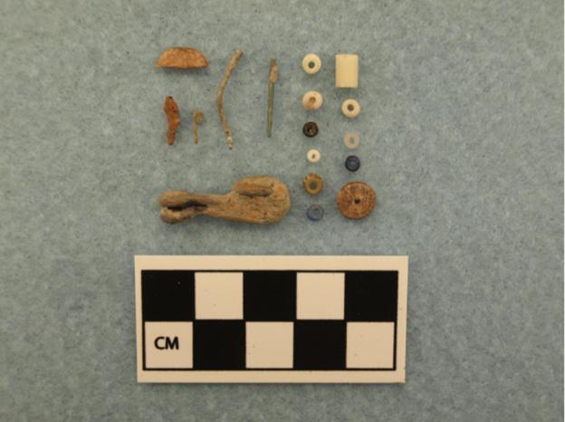 Photograph of fragmented objects on a gray backdrop next to a 10-centimeter scale, divided into one centimeter increments.