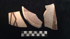 Three pottery sherd fragments. All are light brown color dipped or painted with red streaks. Photograph is on black velvet with black and white centimeter bar below the pottery fragments.