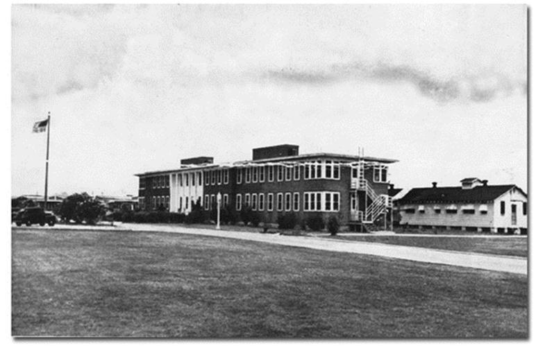 A large two story building with rows of white trimmed windows, an American flag on a flagpole stands out front.