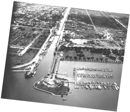 View from above of a canal opening onto a body of water, with a harbor visible.