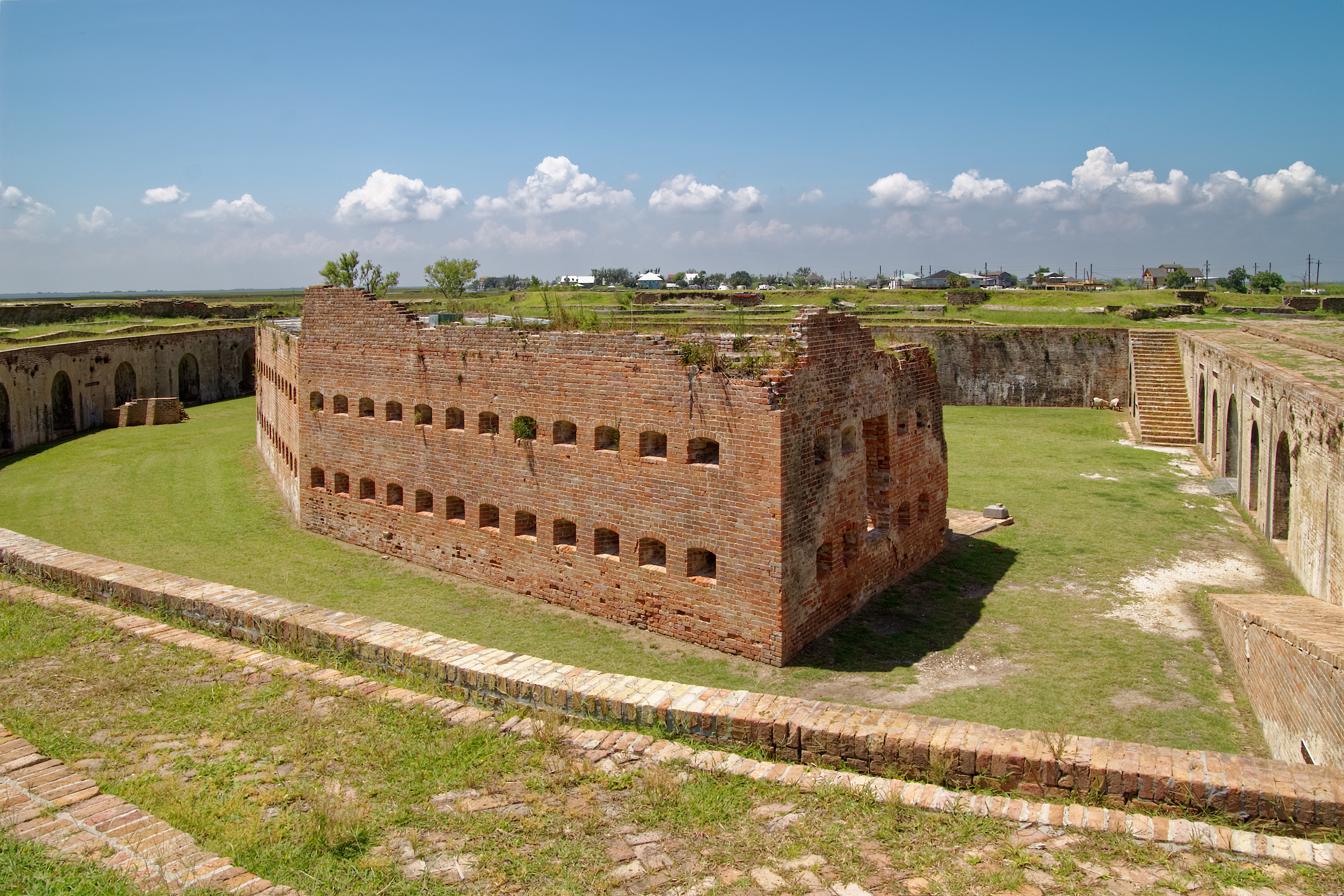 Brick building with rows of deep windows situated on a lawn within a walled fort.